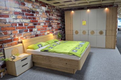 Schlafzimmer Front Lack Taupe, Front mit Aktzenteinlage Balkeneiche. Bestehend aus: Schrank 6türig mit Kranz und Beleuchtung B 304 x H 231, Bettanlage mit schwebendem Fußteil und stehenden Konsolen. sowie 2 LED Flex Leuchten. Bett 180 x 200 cm. Ohne Deko.