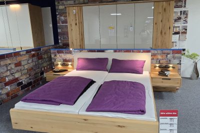 Schlafzimmer in Astkernbuche massiv, Türen Glas Champagner. Bestehend aus: Drehtürenschrank B 300 cm mit Schubkasten- und Wäschebodeneinsatz sowie 6 LEDs im Oberboden Bett 180 x 200 cm mit Unterboden-Bettkasten, LED-Flexleuchtenpaar und LED-Kopfteilbeleuchtung Nachtkommoden Paar am Paneel mit 1 Schubkasten, 