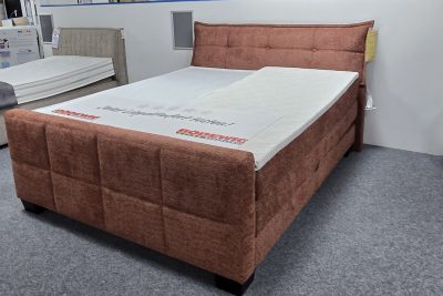 Boxspringbett 180 x 200 cm im Stoff kupferfarben inklusive Matratzen H2 und H3 und 2 Topper. Elektrisch verstellbar Kopf und Fußteil per Funkfernbedienung sowie Stauraum.