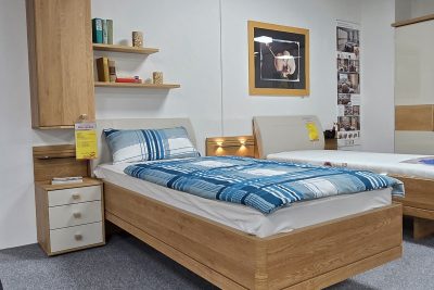 Komfortbett schwebend 90 x 200 cm in Eiche teilmassiv, Kopfteil Stoff in Lederoptik beige. Inklusive Hängeschrank mit Tür, Nachtkommode mit Paneel 40 cm breit und 2 Steckböden 1 x  B 60 cm T 20 cm und 1 x  B 80 cm T 20 cm. Ohne Lattenrost, Matratzen und Deko.